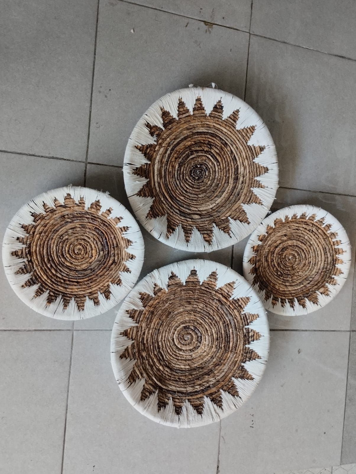 Four handmade woven baskets with sunburst patterns placed on a tiled floor.